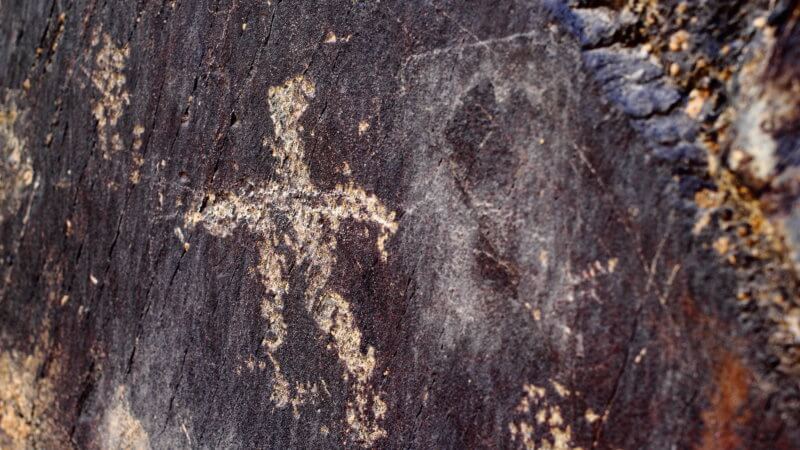 Close-up image of a petroglyph showing the faint outline of a stick-figure man.