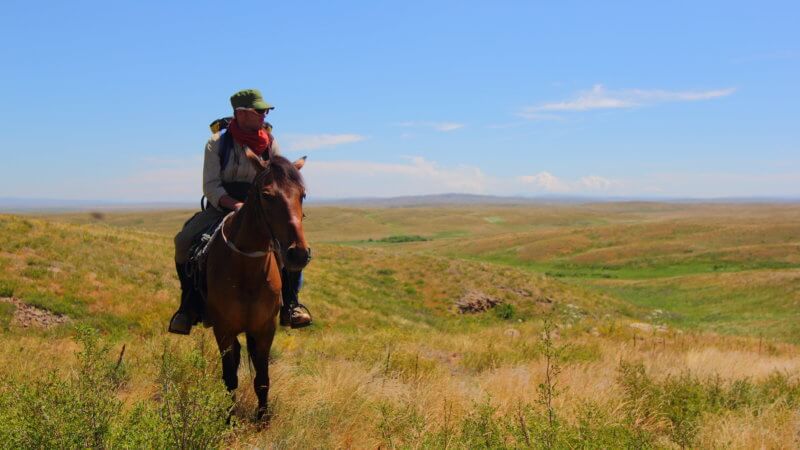 Man and horse ascending up a grass hill in Kazakhstan.