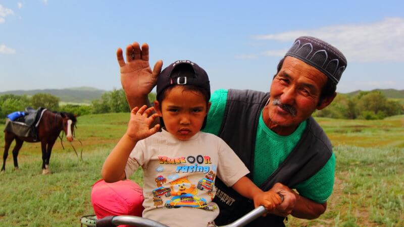 A Muslim Kazakhstan man and boy wave for the camera.