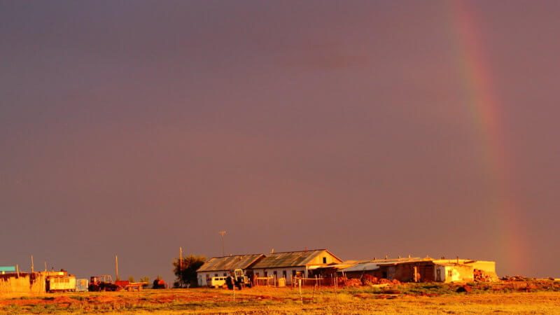 The faint rainbow ends on top of a sunset-soaked east Kazakhstan farmstead.