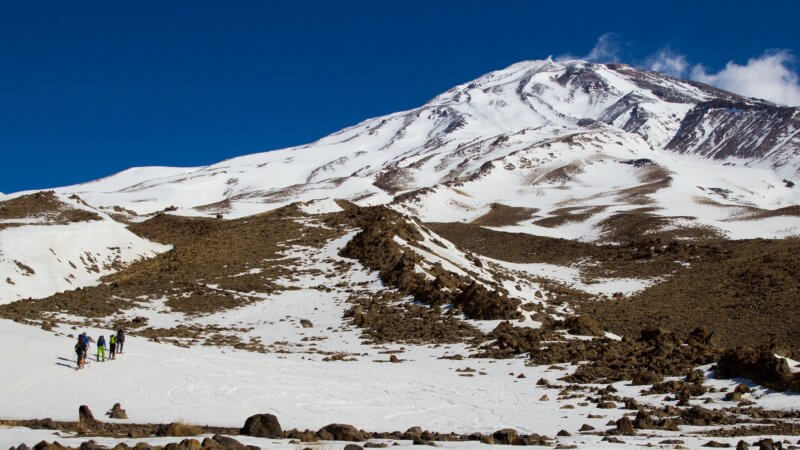 A Mount Damavand photo showing four ski mountaineers heading towards the cloudless summit.