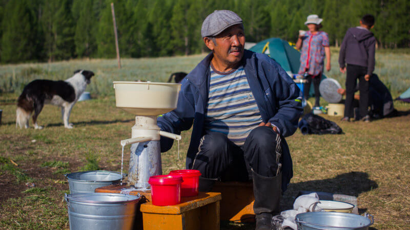A Tuvan farmer crouched down next to a hand-crank milk pasteurising machine.