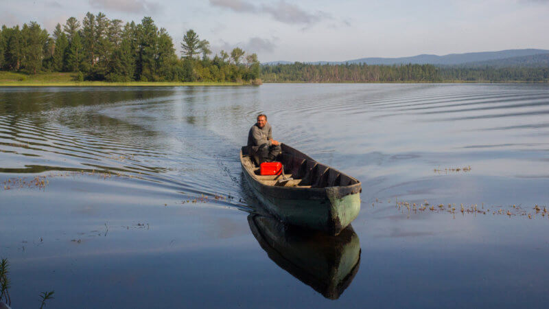 A white Russian man approaches an island in a motorised longboat in Azas Lake, Tuva.