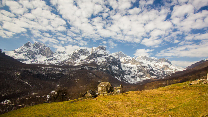 Wide angle photo with blue skies, snowy peaks and grassy farm.
