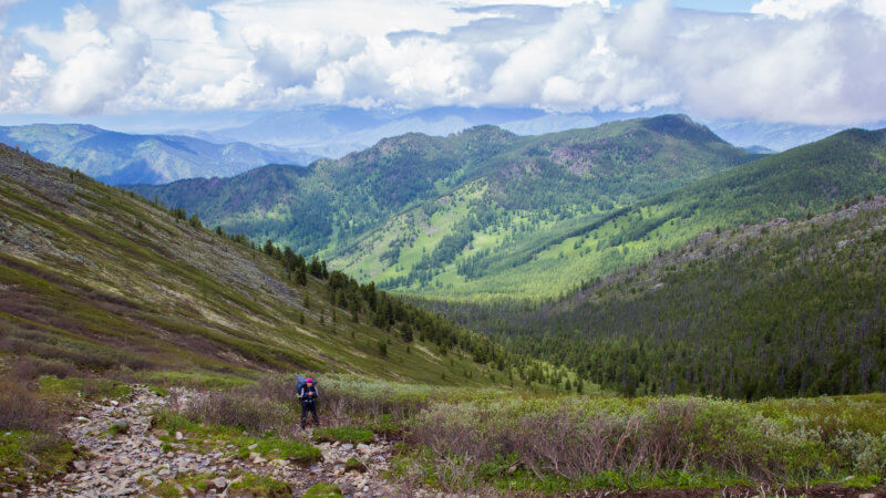 Wide view of a hiker ascending a hill out of a remote alpine valley.