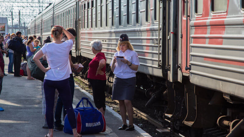 A train conductor stood next to a train carriage and passengers, looking at her paperwork.