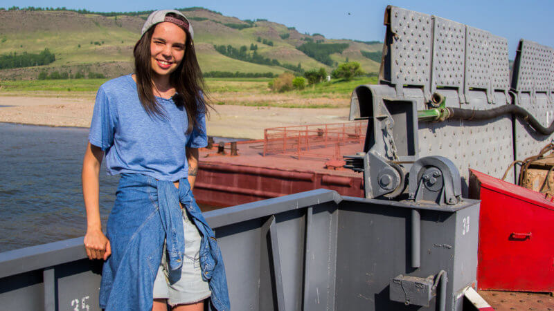A young woman wearing denim poses while resting on the edge of a car ferry.