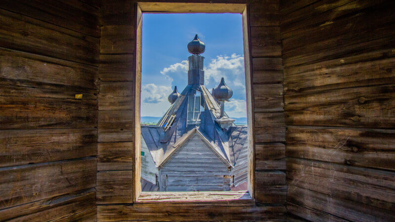 The top of a Russian Orthodox church framed through an old wooden window frame.