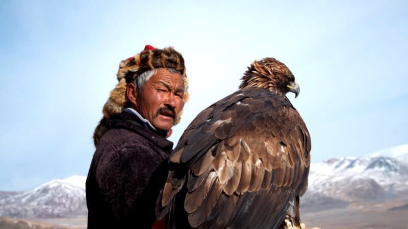 Dalaikhan, a master eagle hunter, holds a hunting eagle on his right arm and looks at the camera.