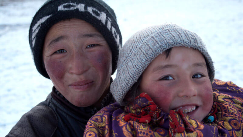 A Kazakh boy lifts up his younger brother for the camera, both playfully smiling.
