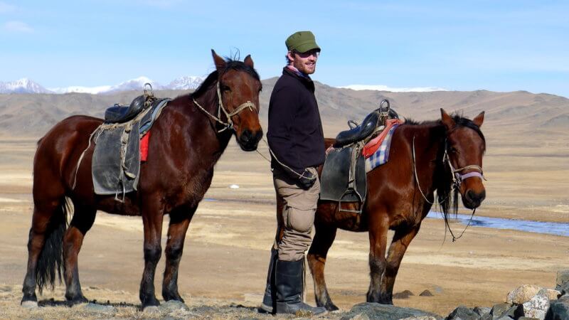 Jamie and two horses pose for the camera on top of a small hill.