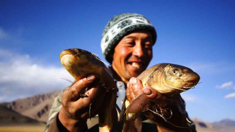 Kyrgyz fisherman smiles as he holds up two large fish caught in the Pamirs.
