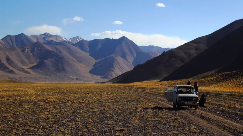 A small white Soviet-era Lada car parked on a dirt track in the Pamir Mountains.