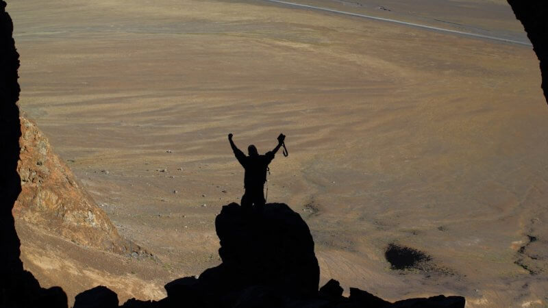 The silhouette of a man at the entrance of a massive cave high in the Pamir Mountains.