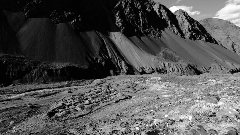 A black and white wide view of the ancient remains of Bazar Dara caravanserai, nestled in a Pamir Mountains valley.