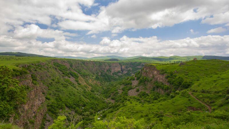 Steep vegetated cliffs of Dashbashi Canyon with the Church of St. George atop a hill on the right.